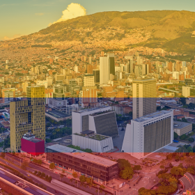 A panoramic view of a city with a mountainous backdrop, featuring tall buildings, residential areas, and landscapes overlaid with color bands—reminiscent of the rich regions where Colombian Coffee Beans are cultivated.