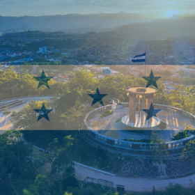 Aerial view of a city monument with the Honduras flag overlay, mountains and buildings visible in the background at sunset, capturing the region famed for its rich Honduras Coffee Beans.